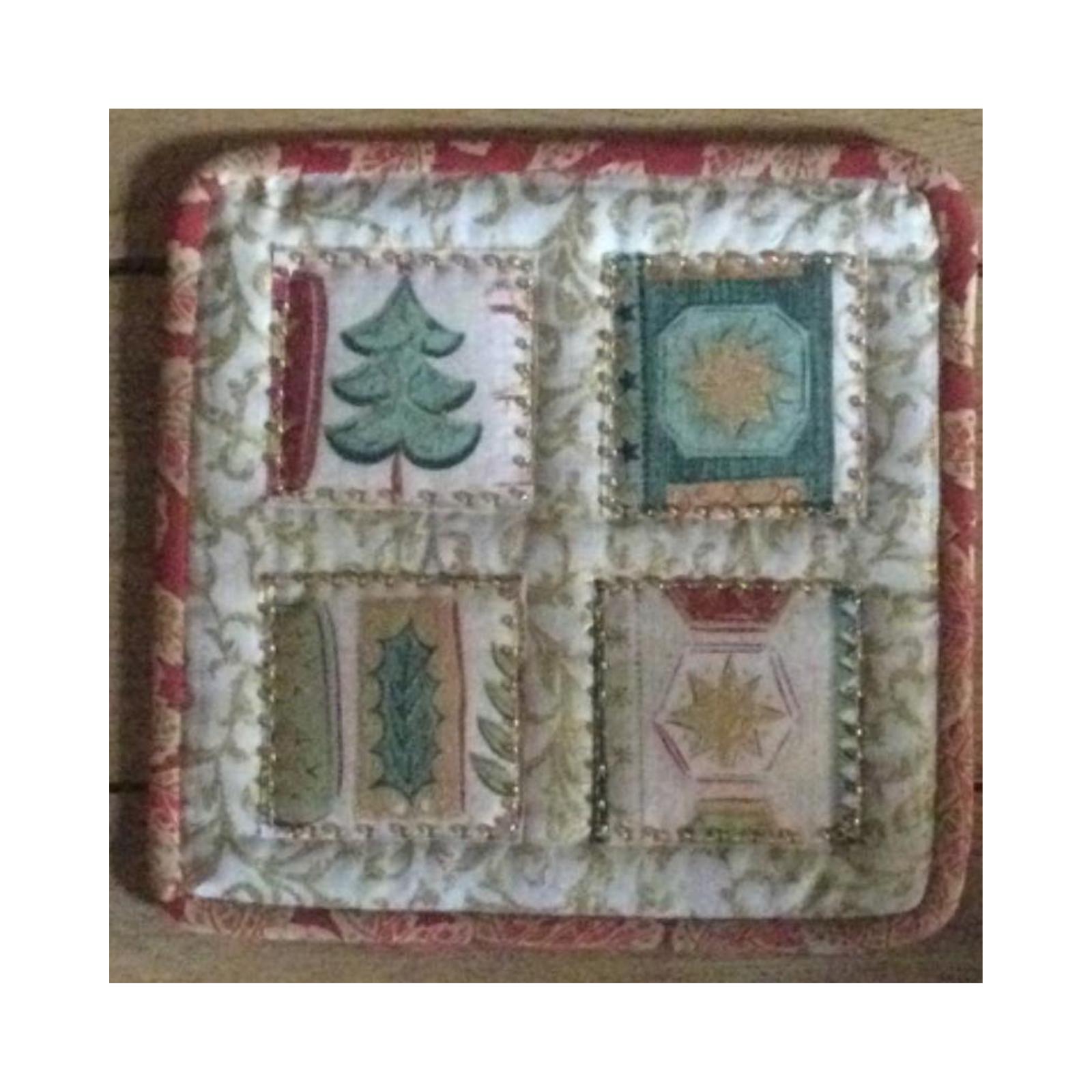 A square quilt with a red border. The quilt is divided into four sections, each with a different design: a green Christmas tree, a blue square with a gold star, a green and brown holly leaf, and a beige square with a gold star. The background is a beige fabric with a floral pattern.