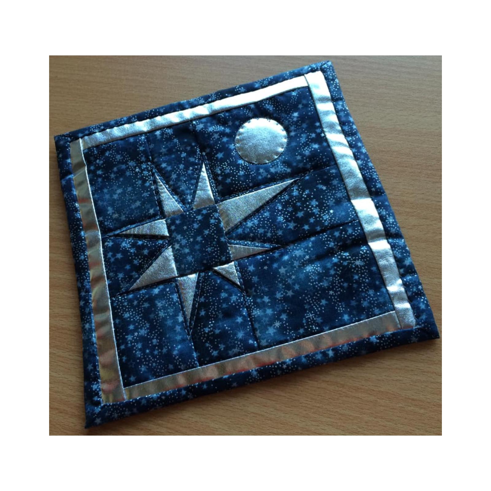 A square quilt with a blue background and a silver border. The quilt features a large, silver star in the center, surrounded by smaller stars. In the top right corner, there is a smaller, silver circle representing the moon. The background is quilted with a subtle, linear pattern.