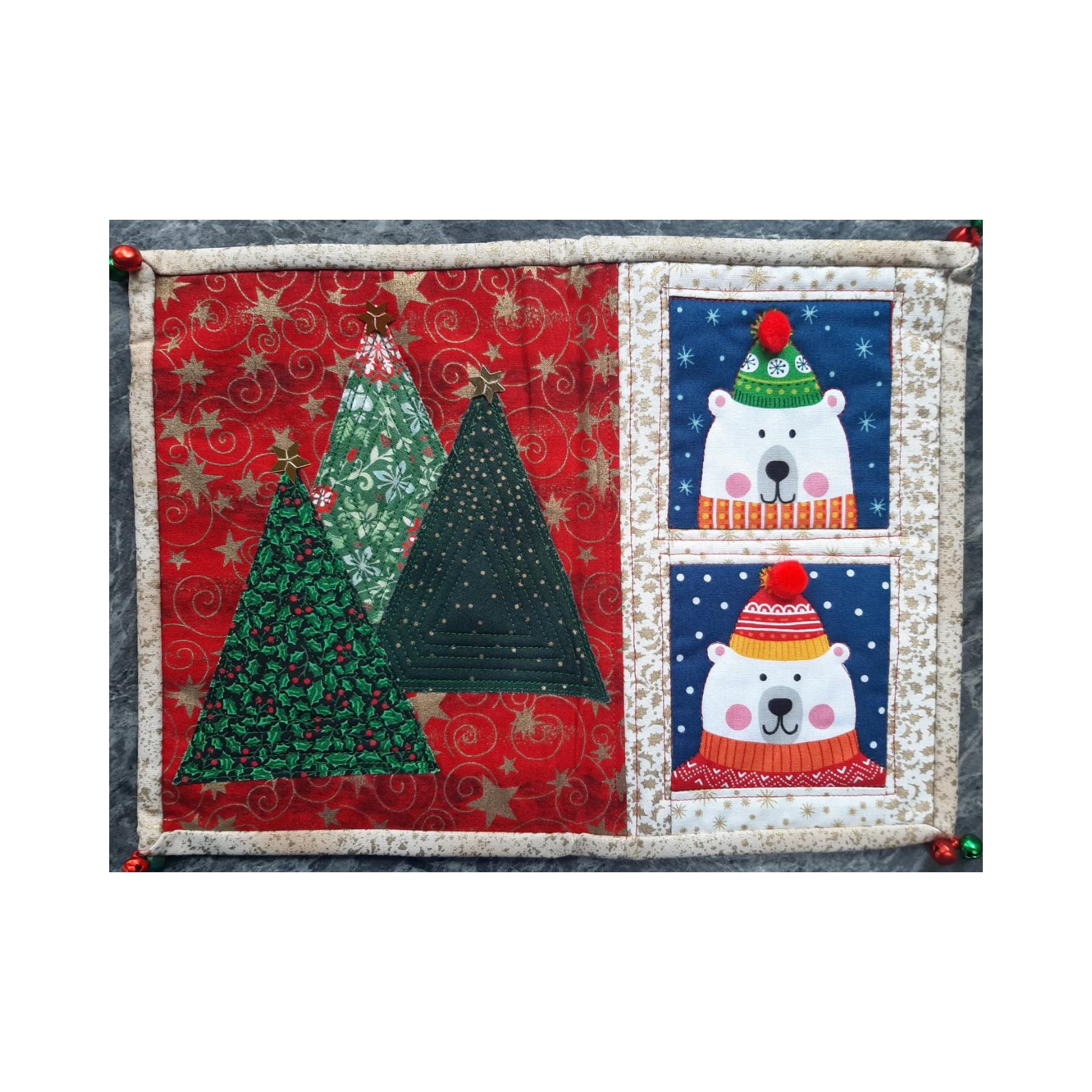 A rectangular quilt with a red background and a white border. The quilt is divided into two sections. The left section features two Christmas trees with ornaments and stars, while the right section shows two polar bears wearing hats and scarves, peeking out of windows.