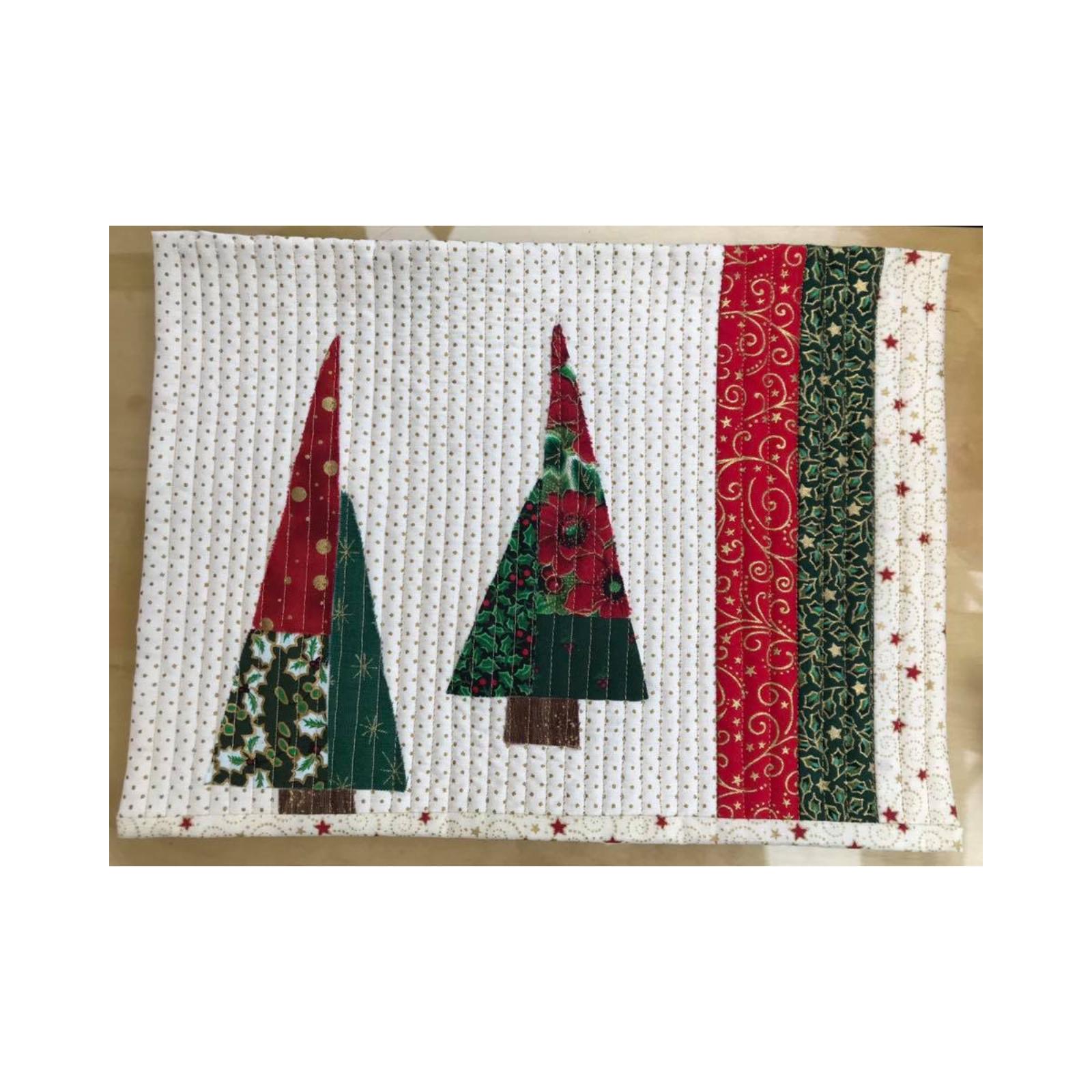 A rectangular quilt with a white background and a red and green border. The quilt features two Christmas trees made up of colorful fabric triangles. The background is quilted with a subtle, linear pattern.