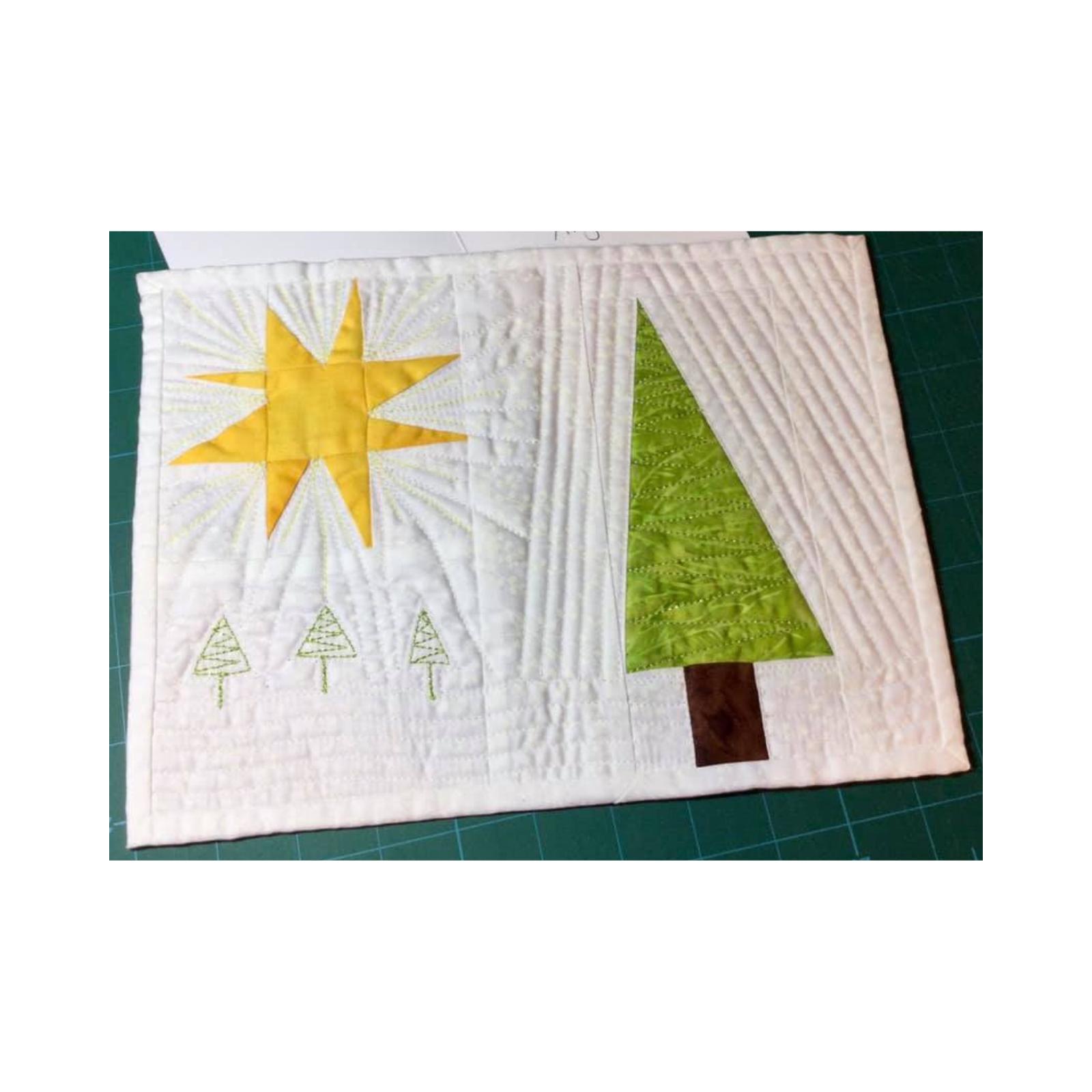 A rectangular quilt with a white background. The quilt features a large, yellow star with rays, a green Christmas tree, and three smaller trees embroidered in green thread. The background is quilted with a variety of lines and stitches.