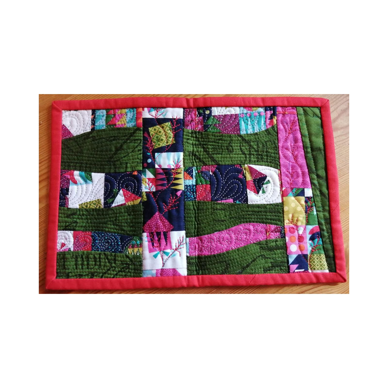 A rectangular quilt with a red border. The quilt features a patchwork design with squares and rectangles in various colors and patterns, including green, pink, blue, and yellow. The background is quilted with a variety of lines and shapes.