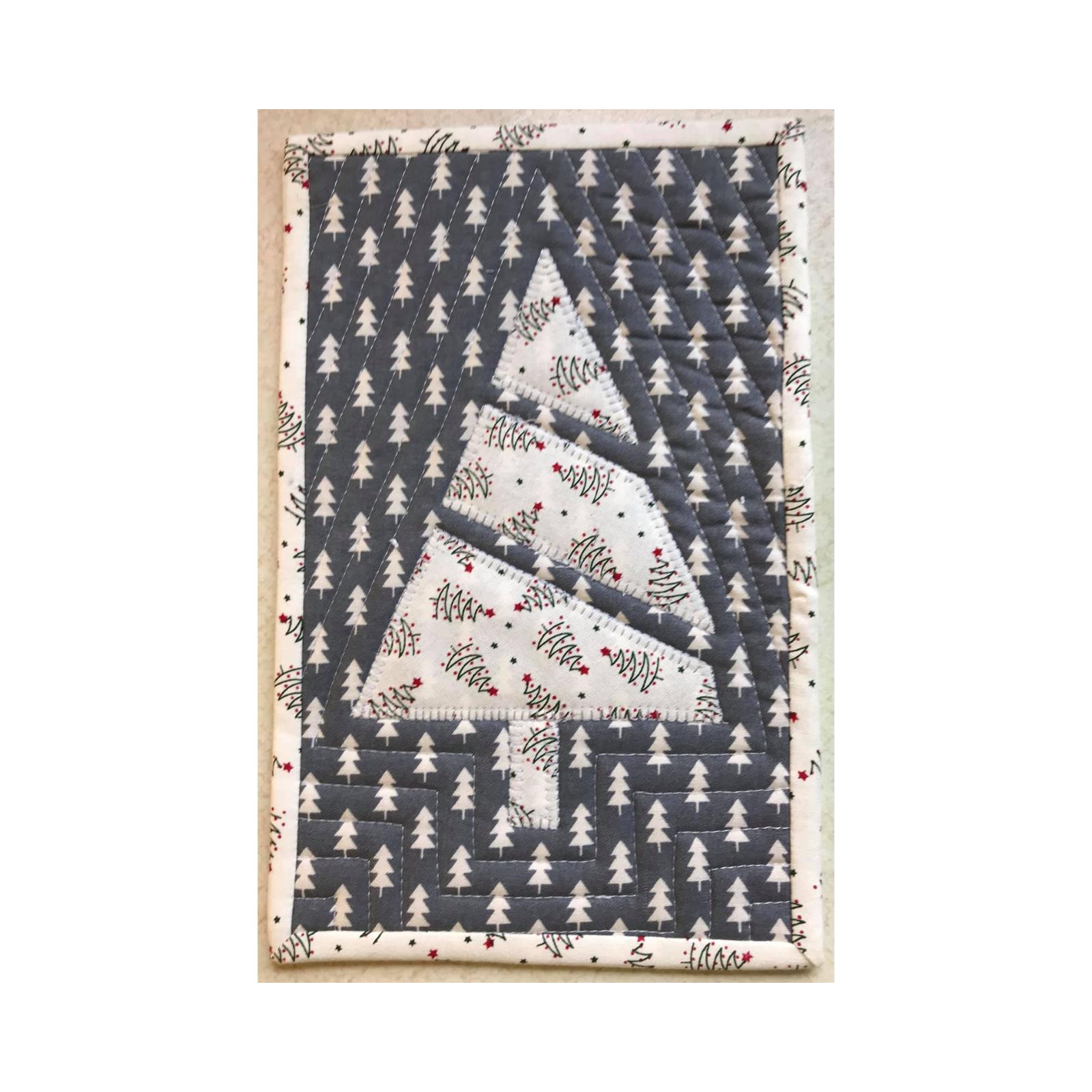 A rectangular quilt with a white border. The quilt features a large, white Christmas tree in the center, surrounded by a dark grey background with a pattern of smaller white trees. The background is quilted with a linear pattern.