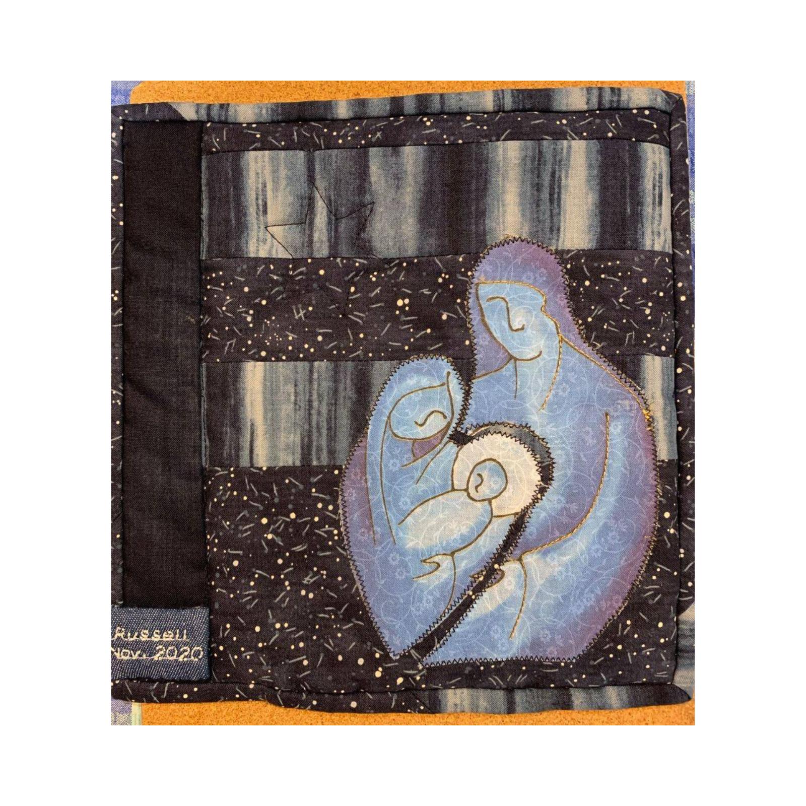 A square quilt with a dark blue background. The quilt depicts the Nativity scene with Mary, Joseph, and baby Jesus. The background is filled with small, white dots, representing stars. The quilt is signed "Russell, Nov. 2020" in the bottom left corner.