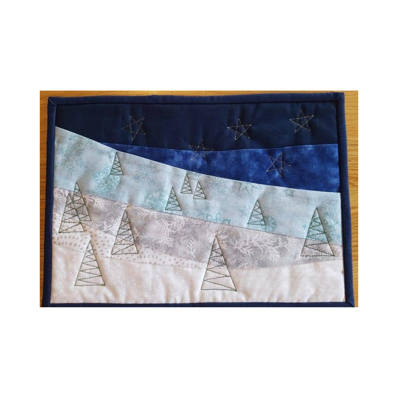 A rectangular quilt with a blue background. The quilt depicts a winter scene with a snowy landscape, small trees, and a starry night sky. The background is quilted with a wavy pattern.