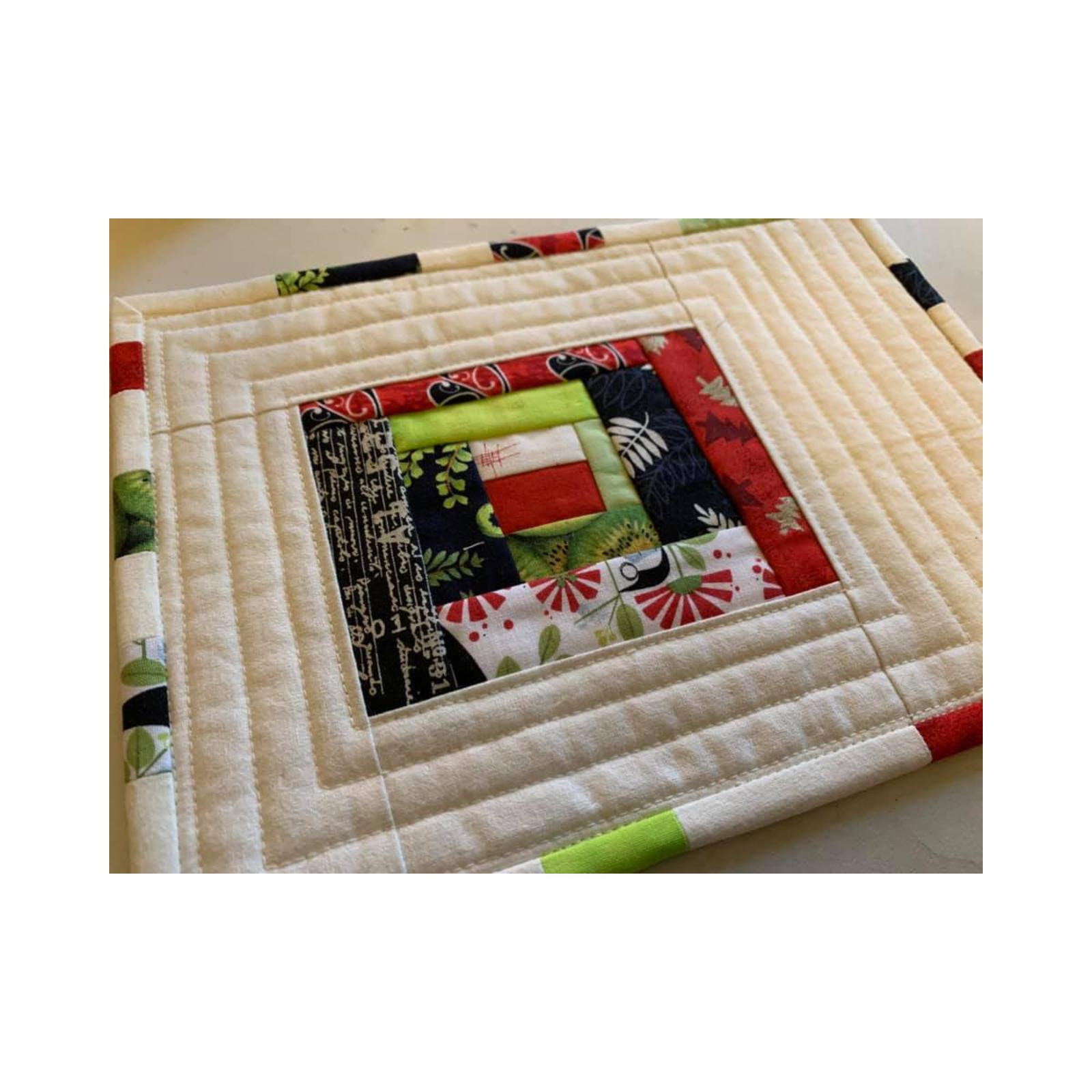 A square quilt with a cream-colored background and a colorful border. The center of the quilt features a patchwork design with squares in various colors and patterns, including red, green, black, and white. The background is quilted with horizontal lines.