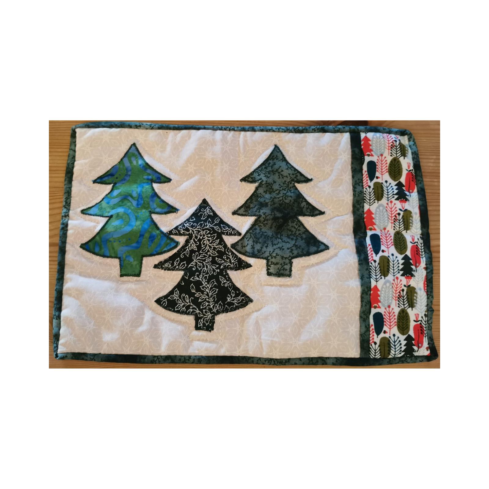 A rectangular quilt with a white background. The quilt features three Christmas trees in different shades of green and blue. The background is quilted with a subtle, linear pattern. On the right side of the quilt is a vertical strip of fabric with a pattern of trees and leaves.