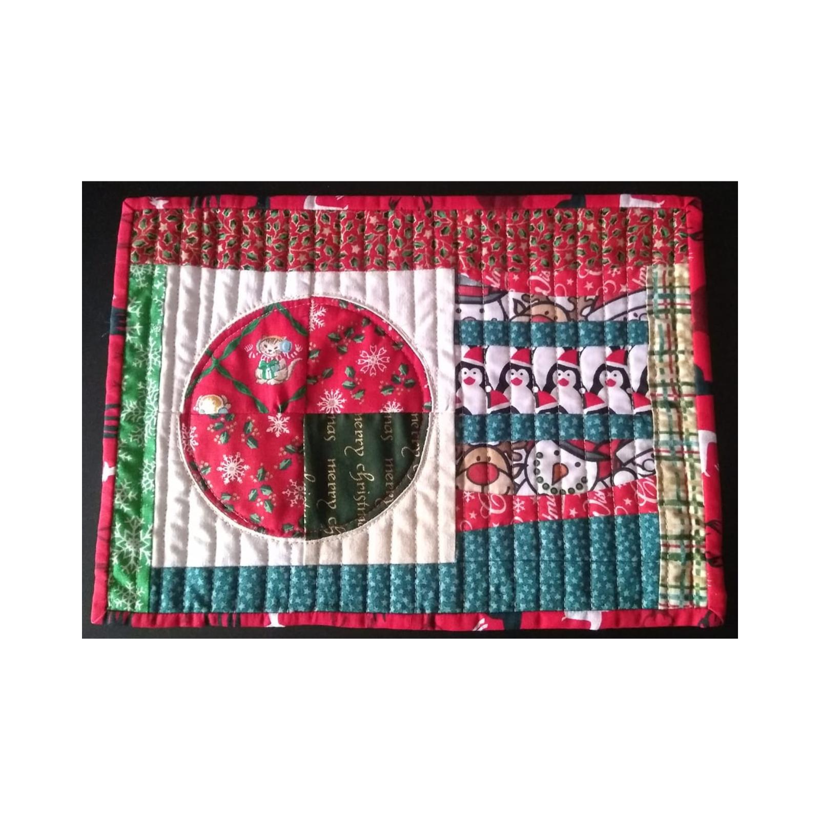 A rectangular quilt with a red border. The quilt features a patchwork design with different Christmas-themed fabrics. There's a circular section with a Christmas pudding, a section with penguins, and another with a snowman. The background is quilted with a linear pattern.
