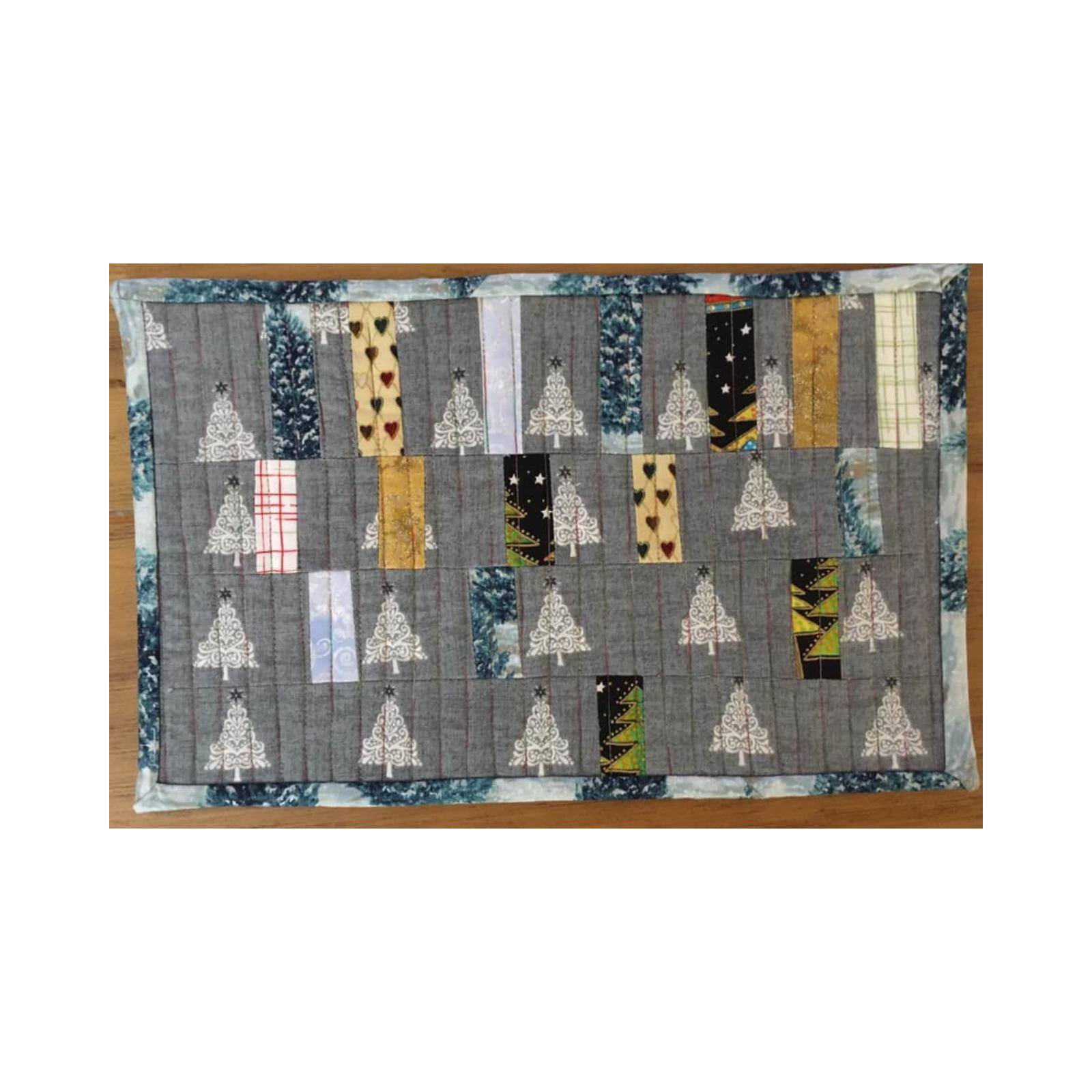 A rectangular quilt with a gray background and a blue border. The quilt features a patchwork design with small squares of different fabrics, including some with Christmas tree patterns. The background is quilted with a subtle, linear pattern.