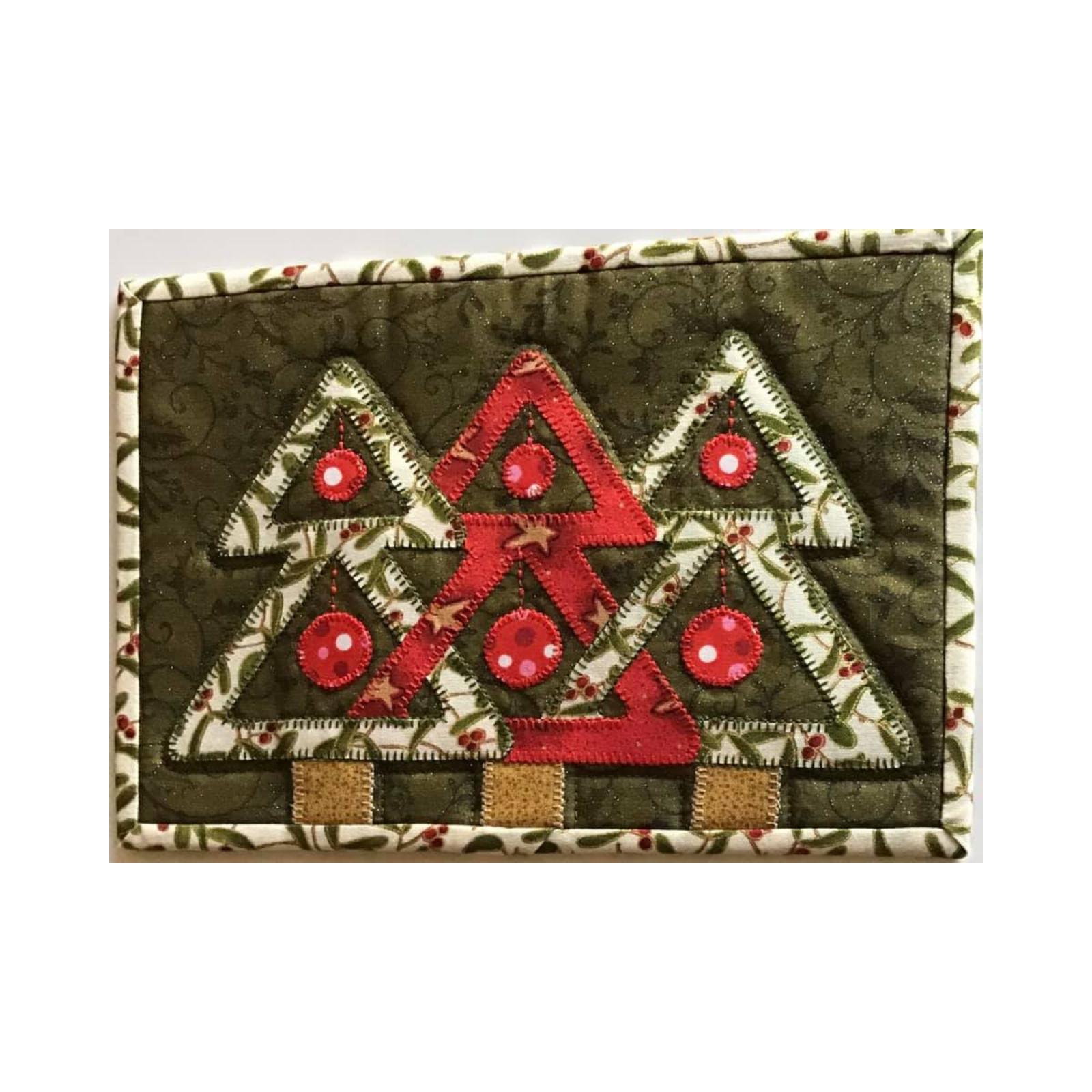 A rectangular quilt with a green border. The quilt features three Christmas trees made of green and red fabric. The trees are decorated with ornaments and have brown trunks. The background is a green fabric with a pattern of small leaves and berries.