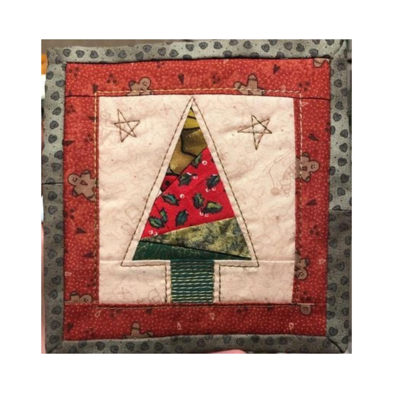 A square quilt with a red border. The quilt features a Christmas tree made up of colorful fabric triangles, with a green trunk. The background is a cream-coloured fabric with a pattern of gingerbread men and stars.