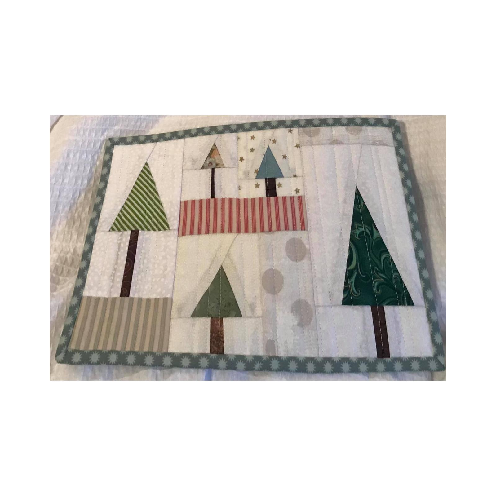 A rectangular quilt with a white background and a green border. The quilt features five Christmas trees of various colors and patterns, including green, red, and blue. The trees are surrounded by a patchwork of different fabrics.