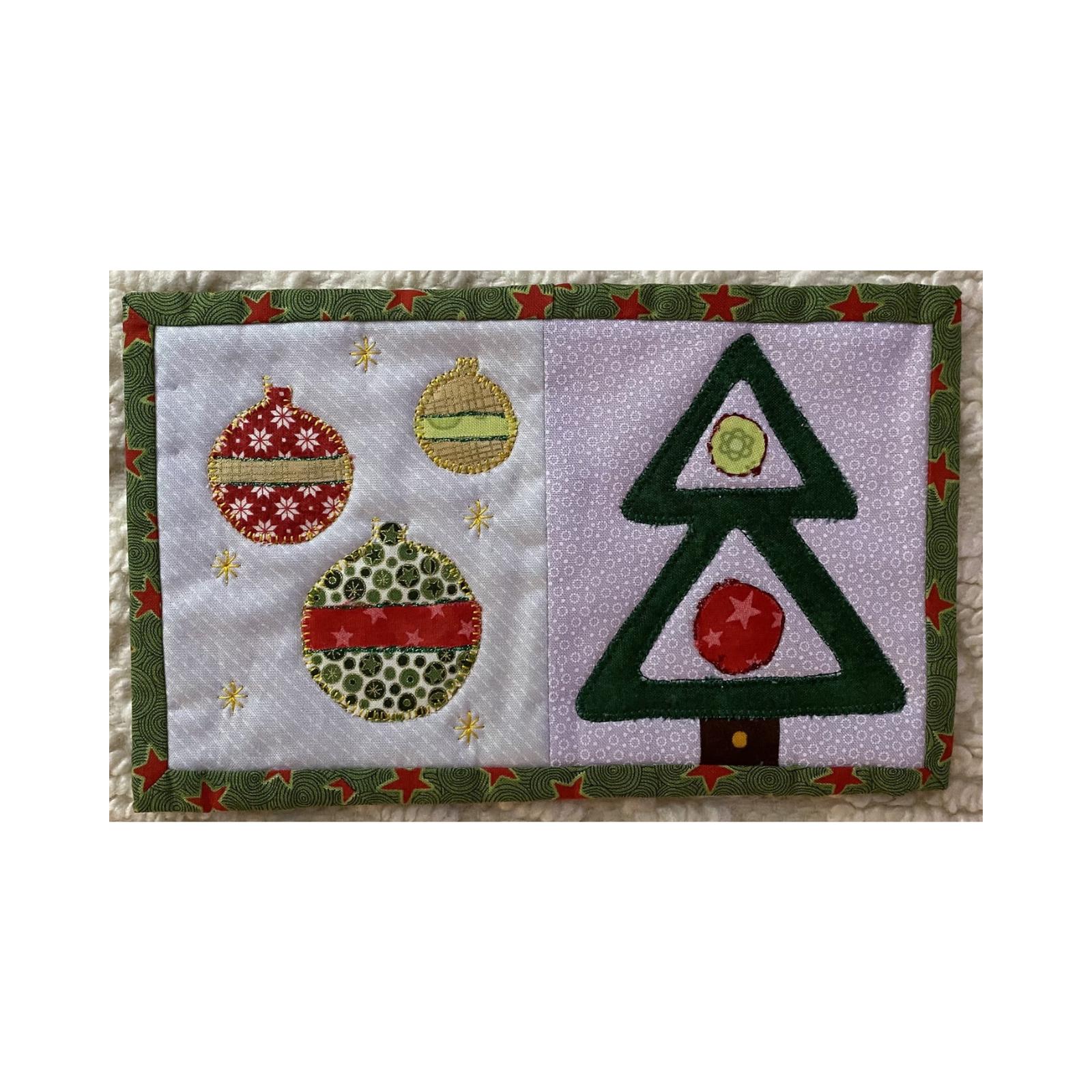 A rectangular quilt with a white background and a green border. The left side features three colorful Christmas ornaments, while the right side shows a green Christmas tree with a red star. The background is quilted with a star pattern.