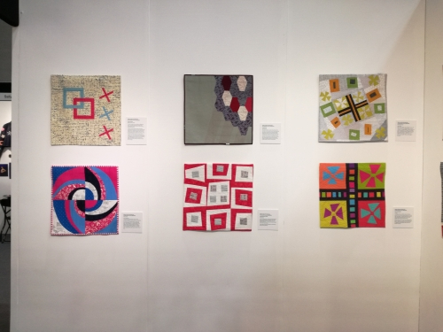 A gallery wall displaying a collection of colourful, abstract quilts.