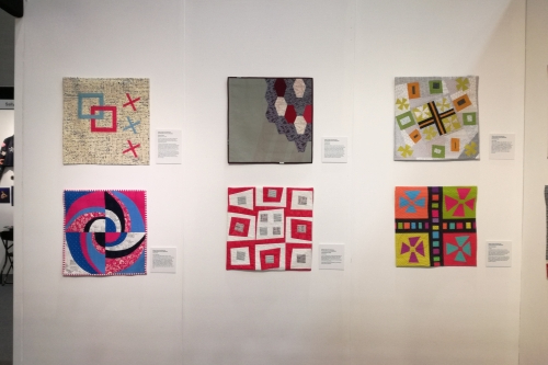 A gallery wall displaying a collection of colourful, abstract quilts.