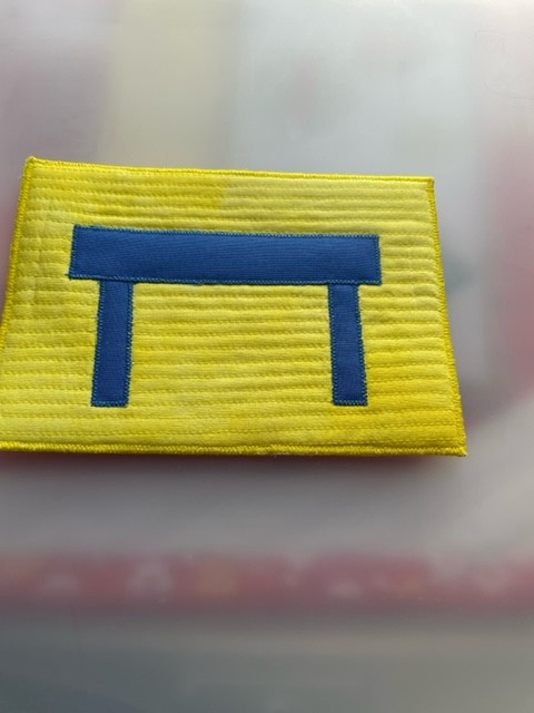 A postcard quilt with a yellow background. The quilt features a simple, blue table shape in the centre. The background is quilted with horizontal lines.