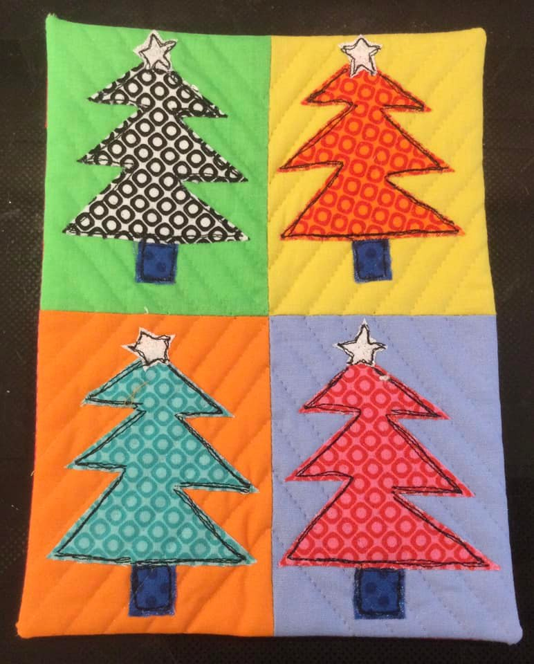 A square quilt divided into four sections, each with a different colored background. On each background, there is a Christmas tree in a contrasting color with a white star on top. The trees are decorated with different patterns, including circles and lines.