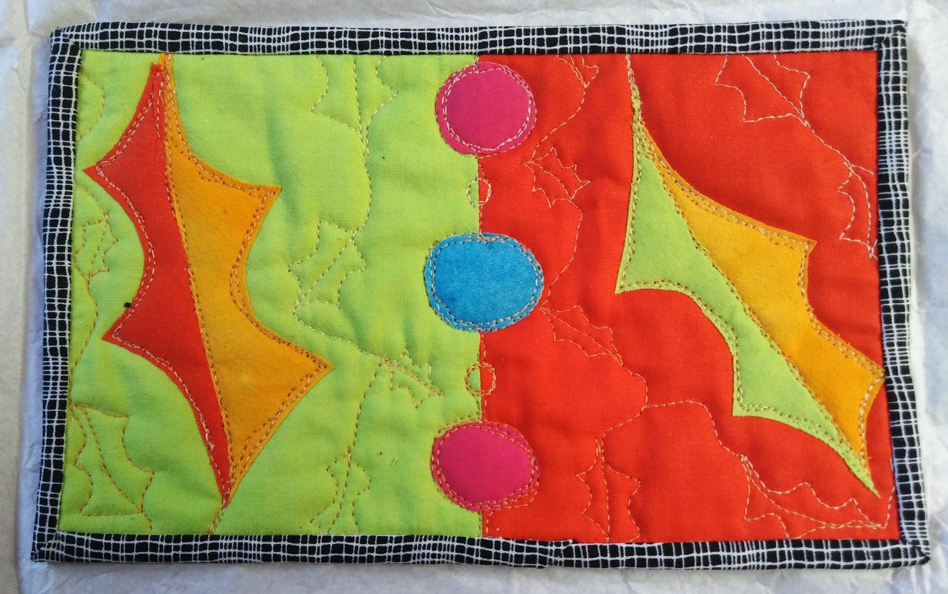 A rectangular quilt with a black border. The quilt is divided into two sections: a green left side with yellow holly leaves and a red right side with pink and blue circles. The background is quilted with a grid pattern.