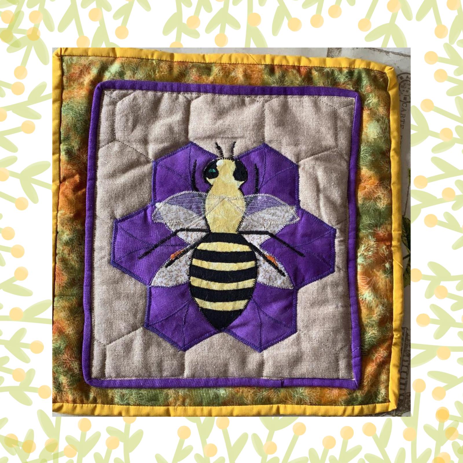 A square quilt with a purple background and a yellow border. The quilt features a large, embroidered bee in the centre, surrounded by a hexagonal pattern. The background is quilted with a linear pattern.