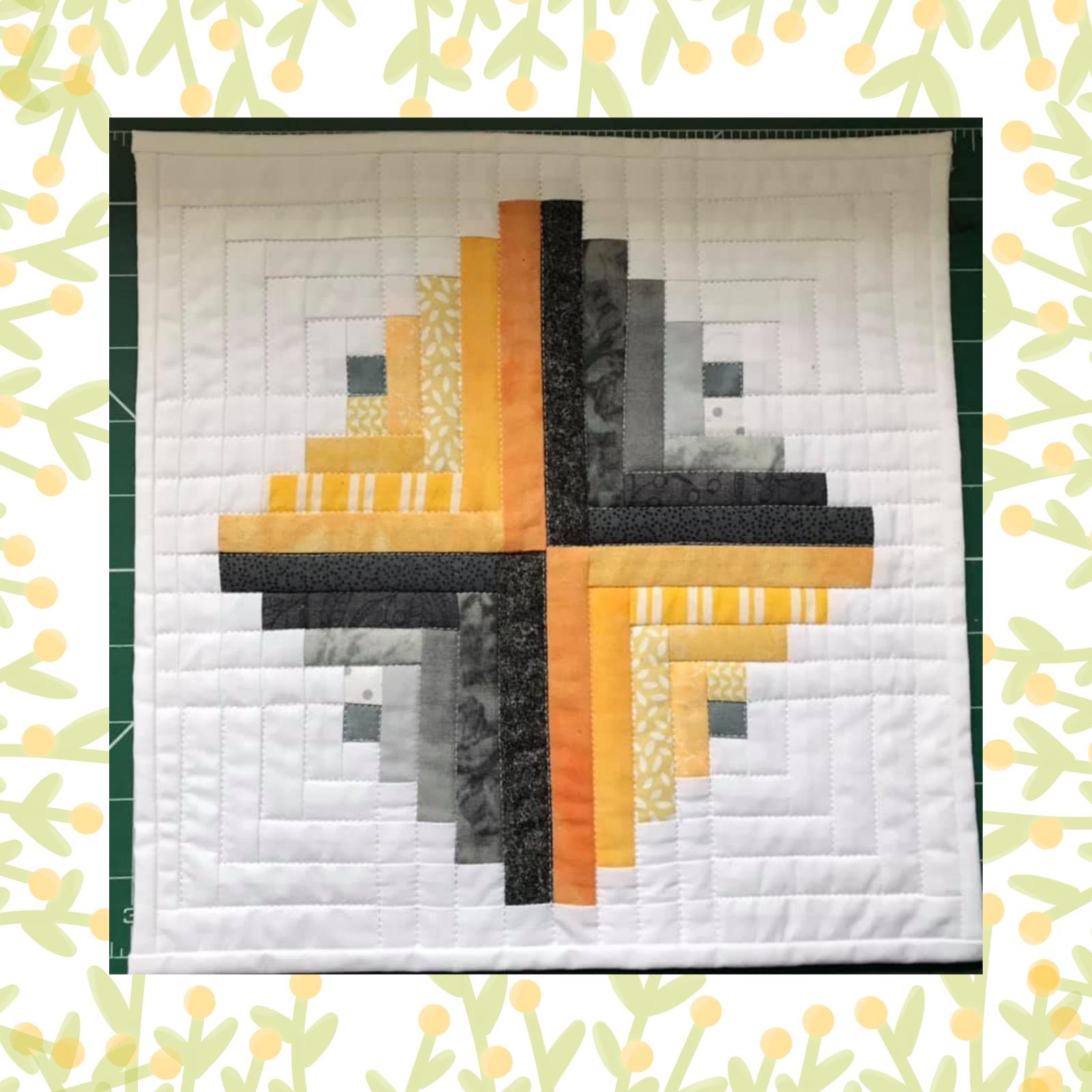 A square quilt with a white background. The quilt features a log cabin pattern with alternating strips of orange and grey fabric. The background is quilted with a subtle, linear pattern.
