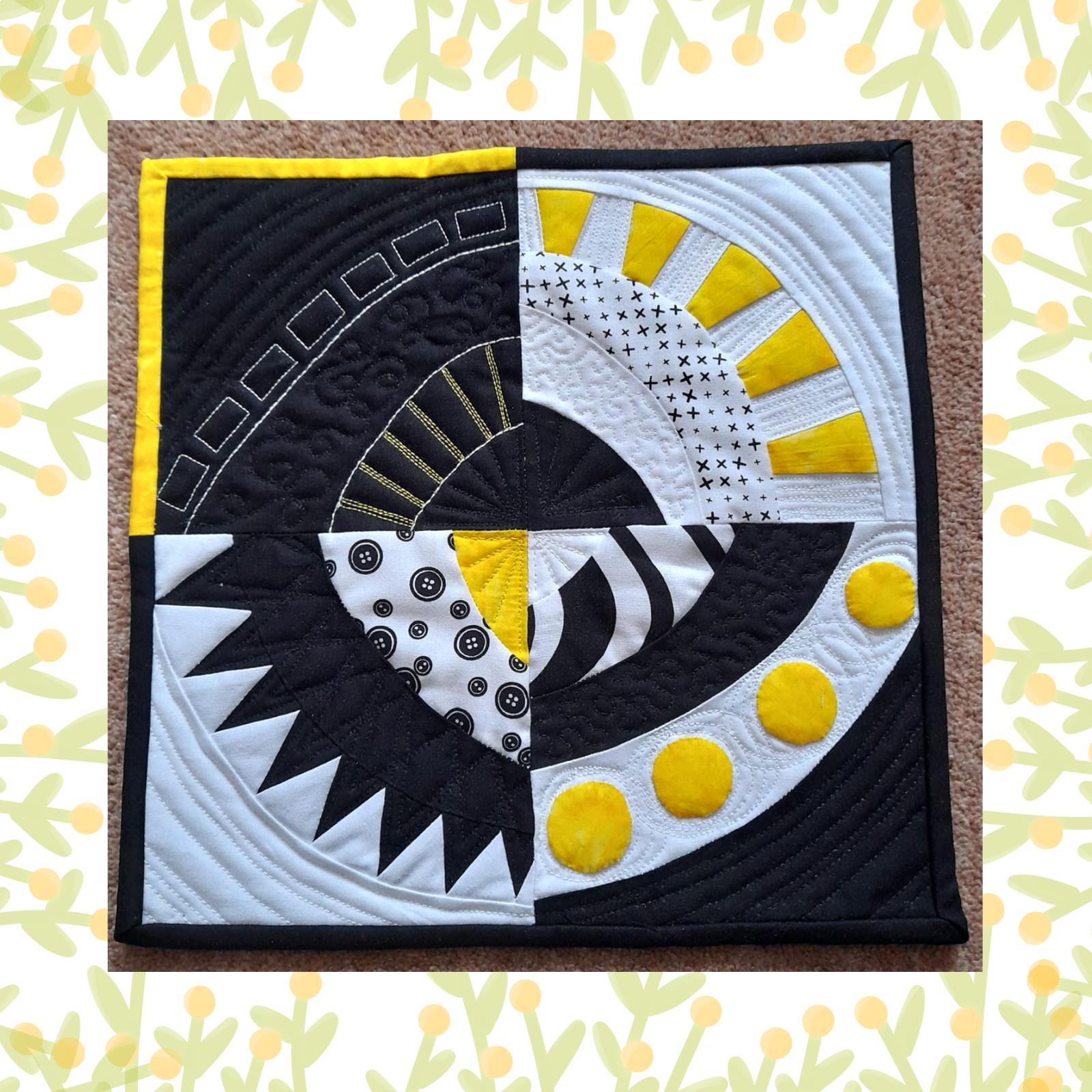 A square quilt with a black background and a yellow border. The quilt is divided into four sections, each with a different pattern. One section has a circular design with buttons, another has a pattern of crosses, and another has a geometric pattern. The background is quilted with a variety of lines and shapes.