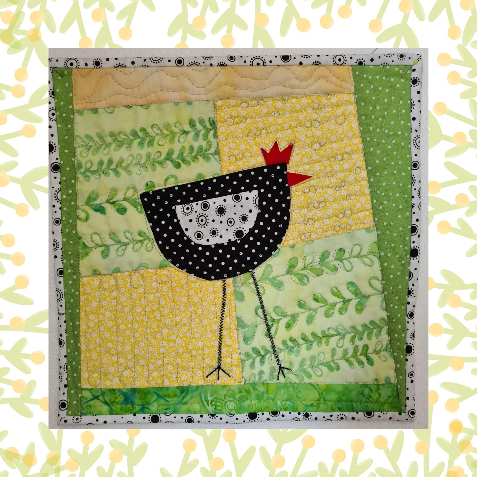 A square quilt with a patchwork design in shades of green, yellow, and black. The quilt features a cute, black chicken with a red comb and white polka dots. The background is quilted with a linear pattern.
