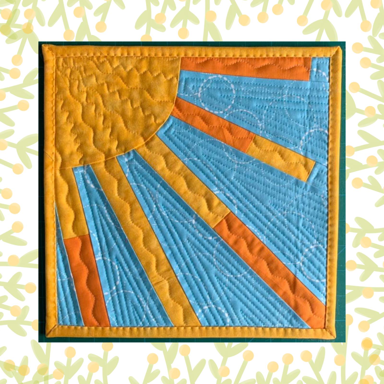 A square quilt with a blue background. The quilt features a large, yellow sun with orange rays extending outwards. The sun and rays are made of fabric pieces sewn together. The background is quilted with a linear pattern. The quilt is framed by a yellow border.