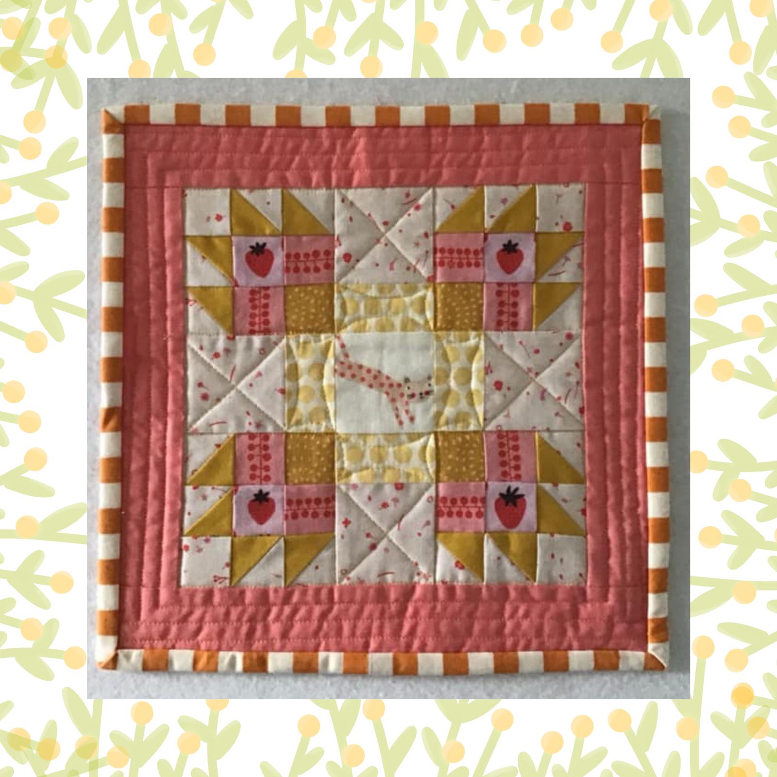 A square quilt with a pink background and a pink border. The quilt features a patchwork design with squares and triangles in pink, yellow, and white. There is a small leopard in the centre. The background is quilted with a linear pattern.