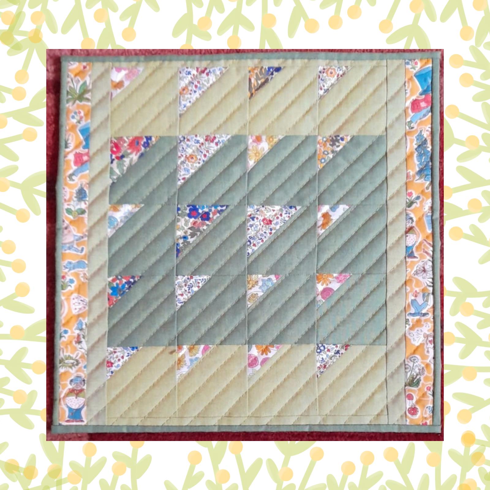 A rectangular quilt with a green background and a yellow border. The quilt features a patchwork design with triangles and squares in various shades of green. Some of the squares have a floral pattern. The background is quilted with a linear pattern.