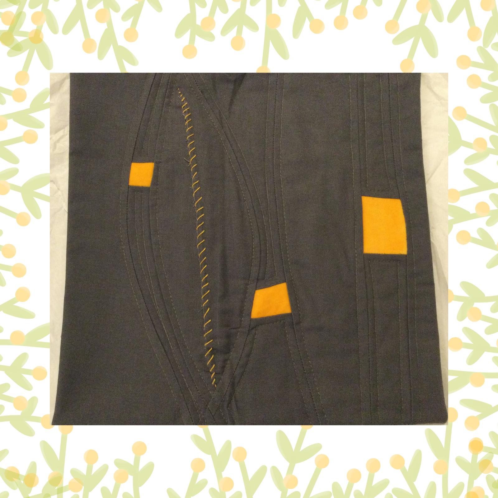 A square quilt with a dark grey background. The quilt features a minimalist design with three yellow squares of varying sizes, arranged asymmetrically. The background is quilted with curved lines.