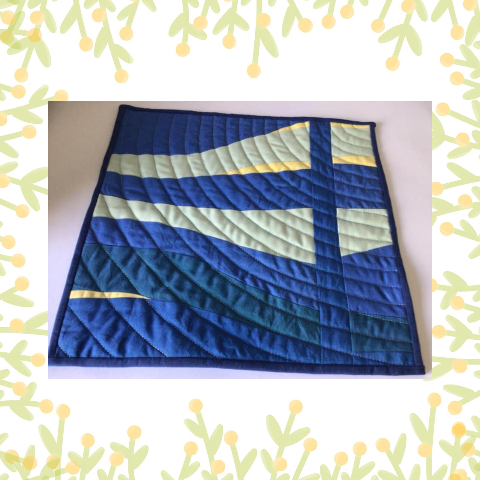 A square quilt with a predominantly blue background. The quilt features a geometric design with curved lines in shades of blue and green, creating a sense of movement and depth. The quilt is framed by a blue border.