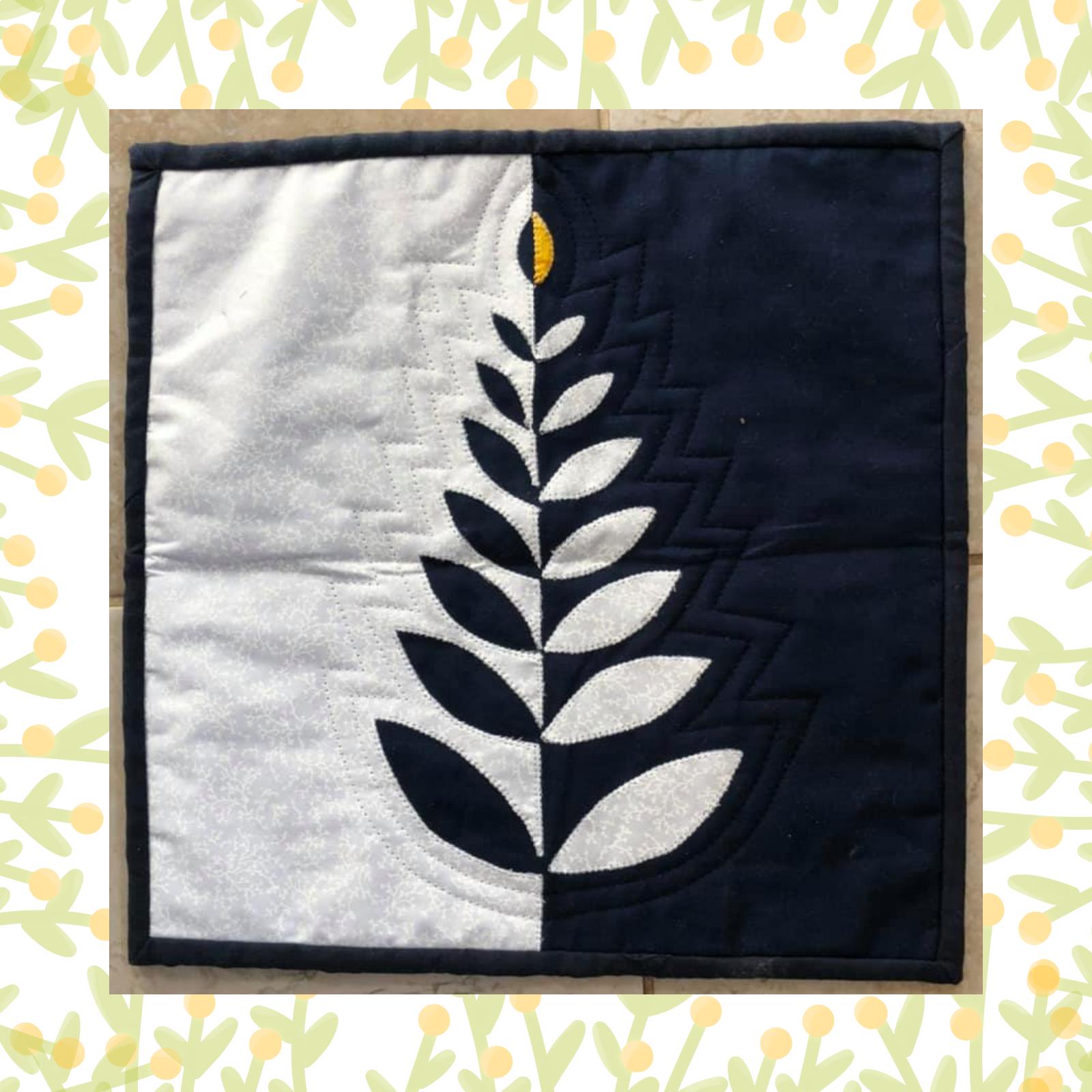 A square quilt with a black and white colour scheme. The quilt is divided into two halves, with a black background on the right and a white background on the left. A stylized fern-like shape, made up of black and white pieces, extends from the centre of the quilt to the edge. The fern has a small, yellow circle at its tip.