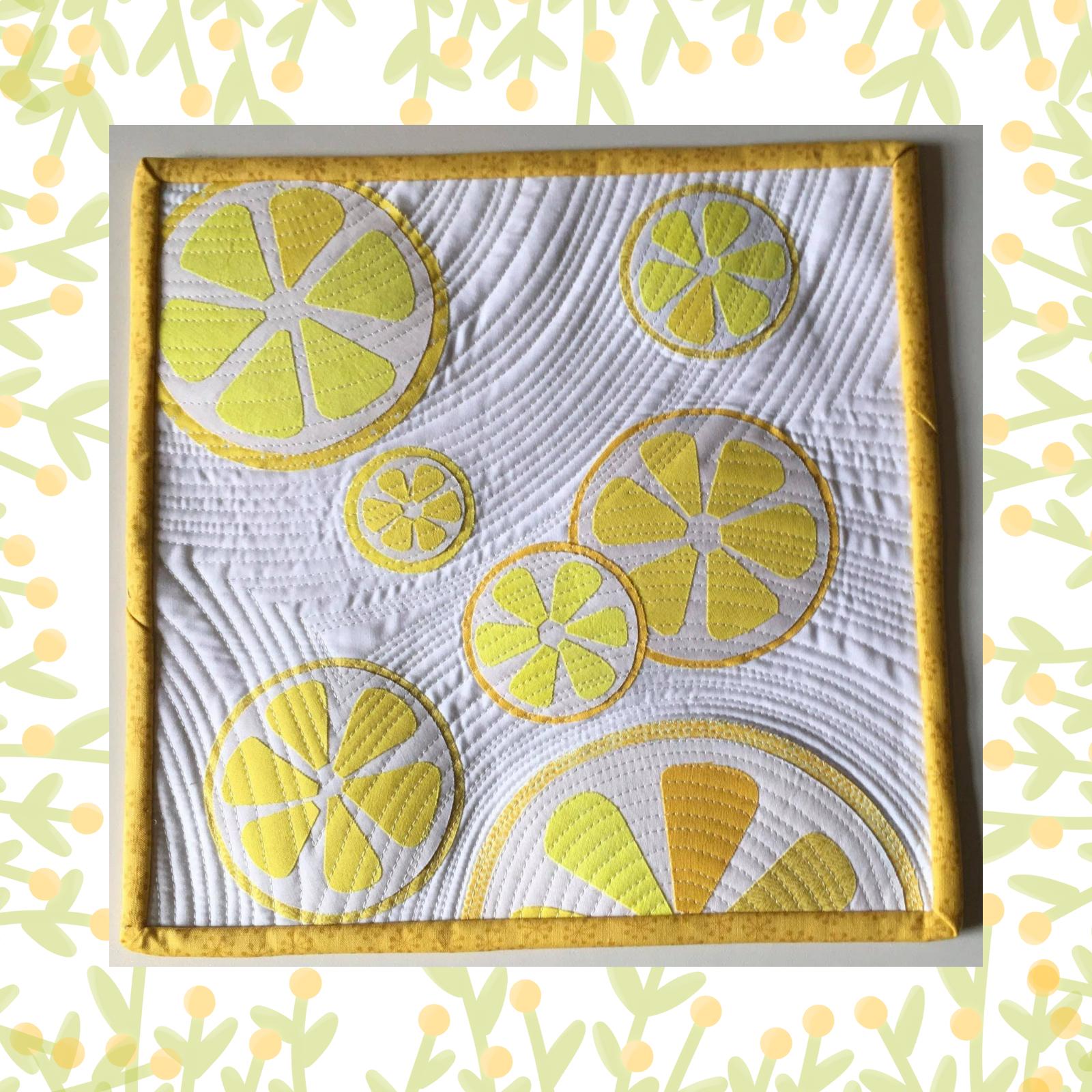 A square quilt with a white background and a yellow border. The quilt features multiple lemon slices in various sizes, all in shades of yellow. The background is quilted with a wavy pattern.
