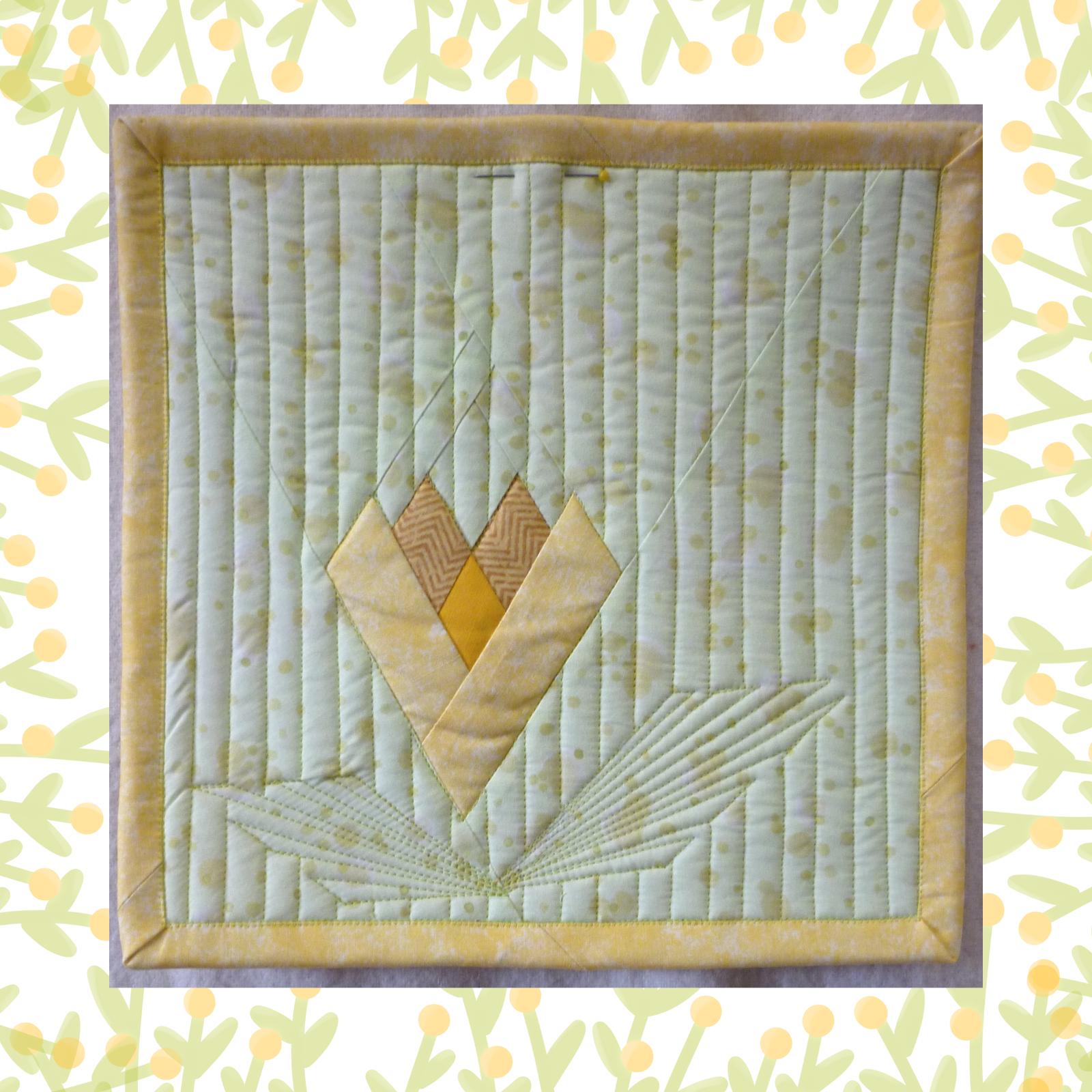 A rectangular quilt with a yellow background and a yellow border. The quilt features a stylized flower design in shades of yellow and brown, with intricate quilting details around the flower. The background is quilted with vertical lines.