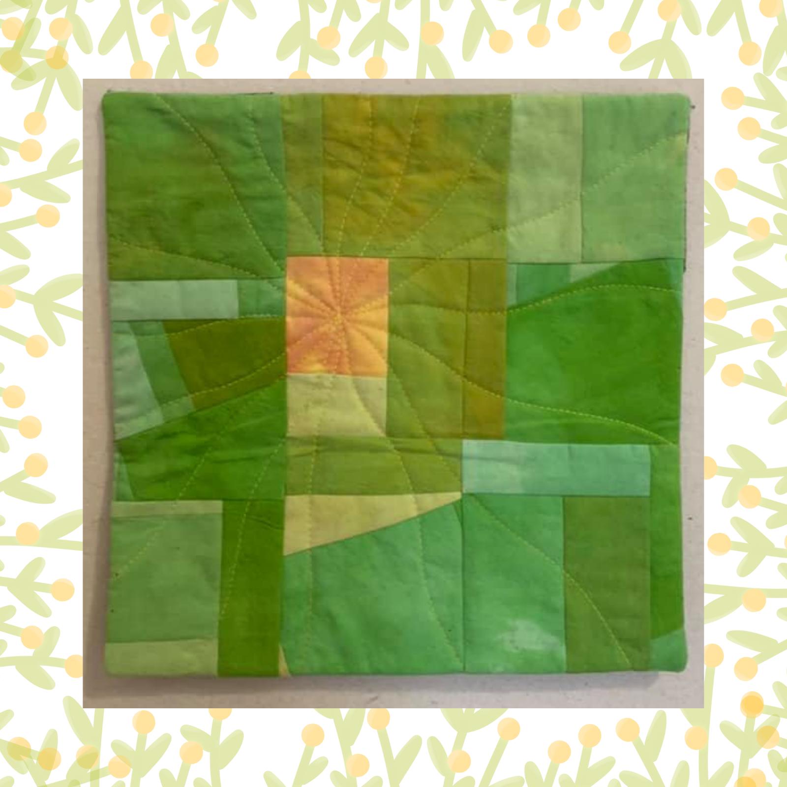 A square quilt with a green background. The quilt features a patchwork design with squares and rectangles in various shades of green and a small, orange square in the centre. The background is quilted with a radiating line pattern.