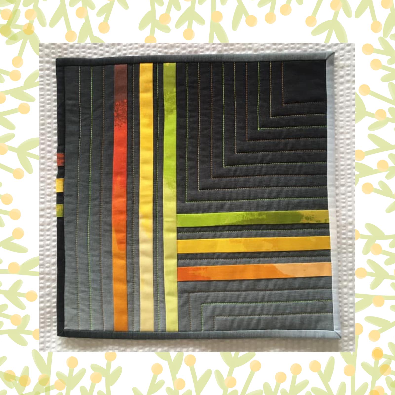 A square quilt with a grey background and a white border. The quilt features a geometric design with vertical stripes of fabric in various shades of orange, yellow, and green. The background is quilted with a linear pattern.