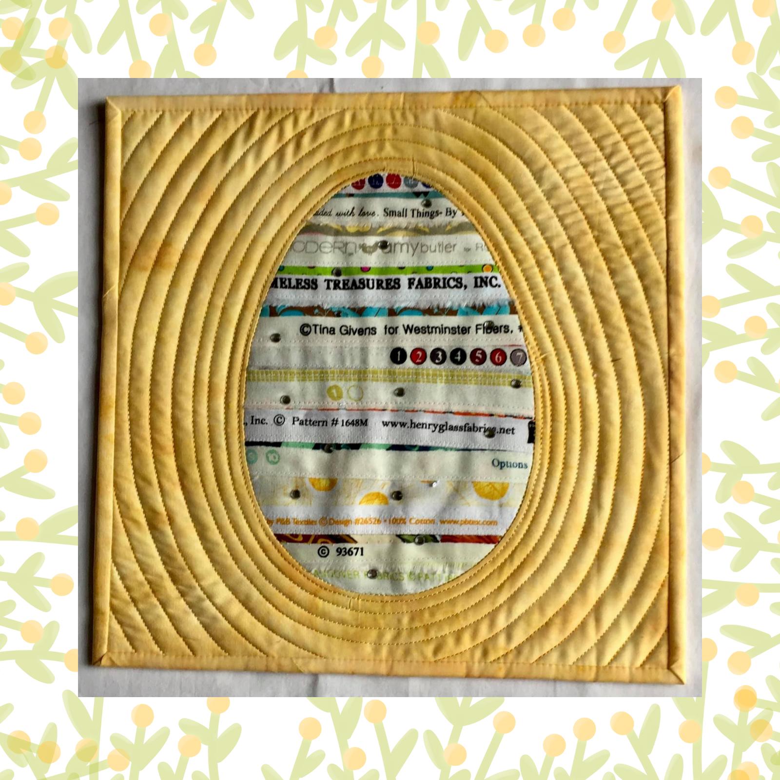 A square quilt with a yellow background. The quilt features a large, circular window cut into the fabric, revealing a colourful, patterned fabric underneath. The background is quilted with concentric circles.