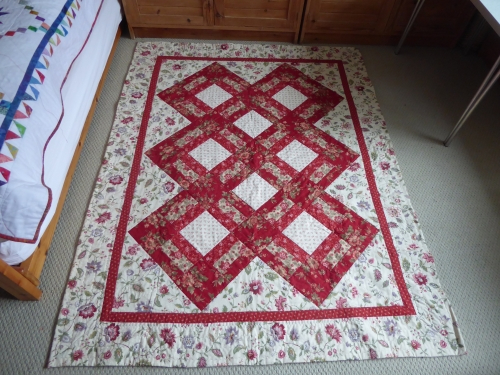 Quilt by Mary Cunningsworth. Red floral interlocking diamond pattern on a light floral fabric background