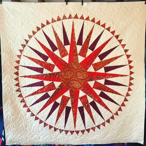 Quilt by Pippa Moss. Large red compass style sun image on a white background