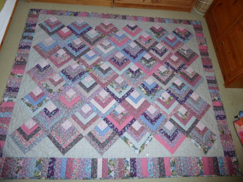 Traditional style quilt by Mary Cunningsworth. Squares made of concentric chevrons and a wide border in pink and blue patterned fabric.