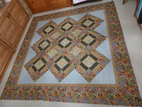 Traditional quilt by Mary Cunningsworth. Large interlocking diamond pattern with large border in a blue, brown and green leaf patterned fabric