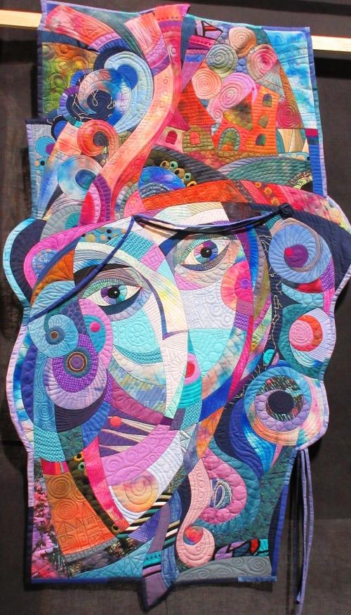 Abstract quilt with irregular shape depicting a woman's face in pink, blue and beige shapes