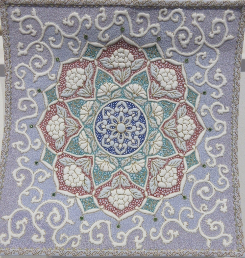 Square quilt with light purple background and a mandala design in red, green, blue and beige