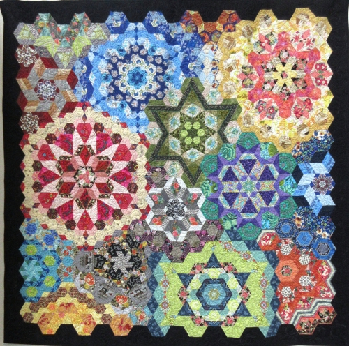 Quilt with black border made of multi-coloured hexagonal and triangle pieces