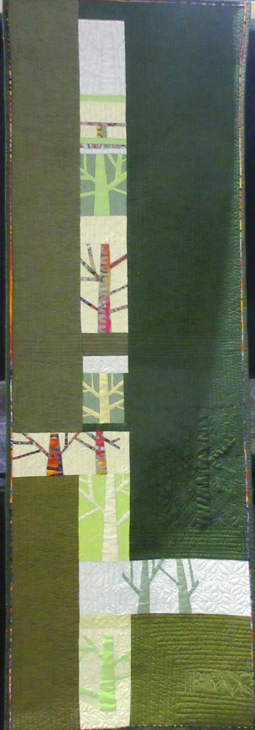 Long narrow quilt depicting several leafless trees on a green background