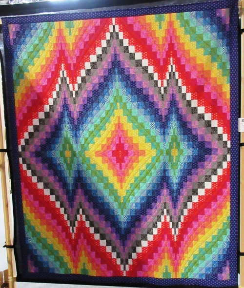 Quilt made of many small squares in rainbow colours in a design of concentric diamond shapes