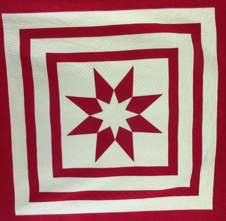 Square quilt with concentric red and white squares and a star in the centre