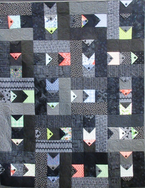 Quilt made of black and grey patterned fabric squares and triangles with a selection of shapes in red, blue and yellow