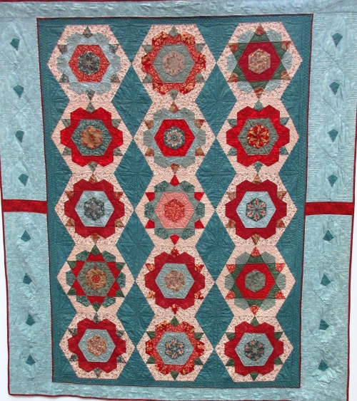 Quilt with light and dark jade green background and 16 red and green rose motifs made of hexagonal and triangle shapes