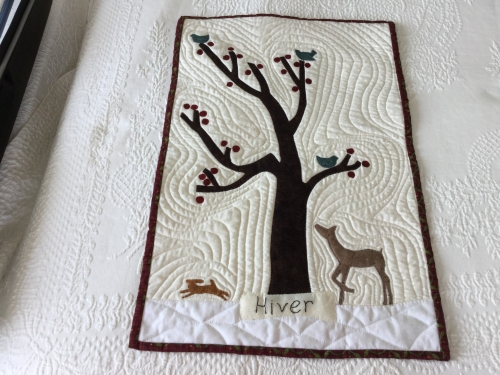 Small quilt laid on a larger white quilt, depicting a tree with animals either side